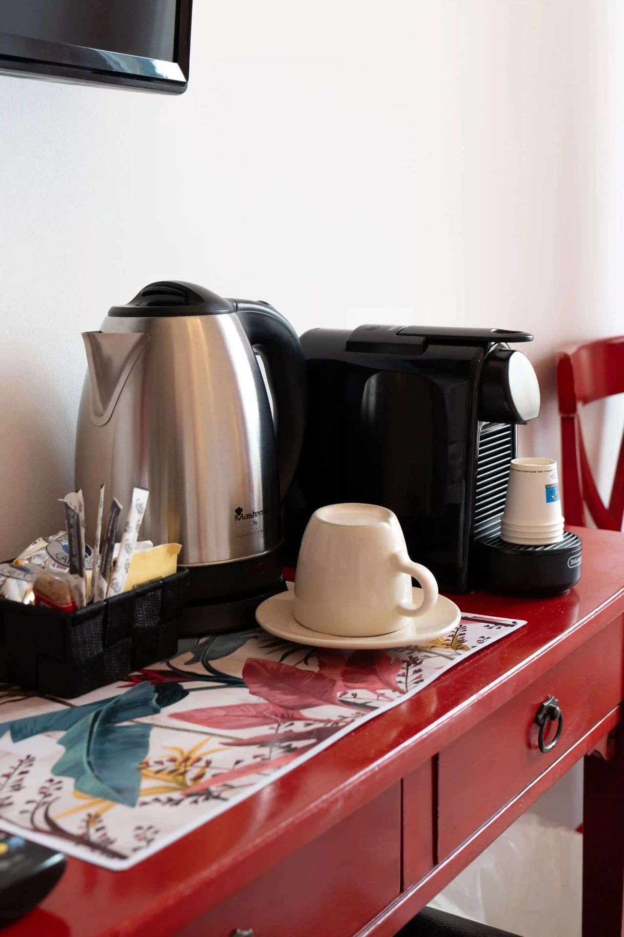 Angolo tè e caffè su scrittoio rosso con bollitore, macchina a capsule e tazza