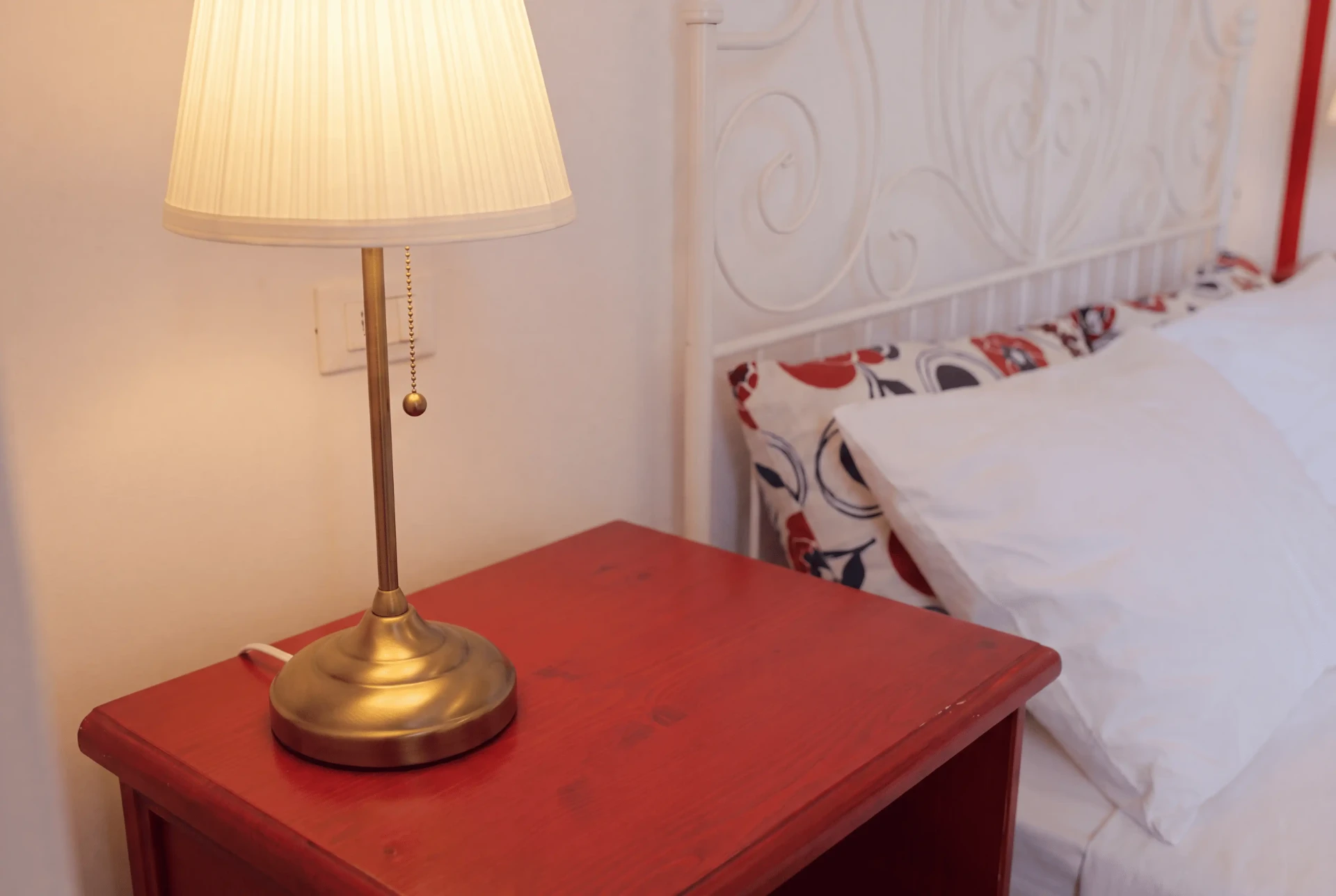 Comodino laccato rosso con lampada in ottone accanto al cuscino