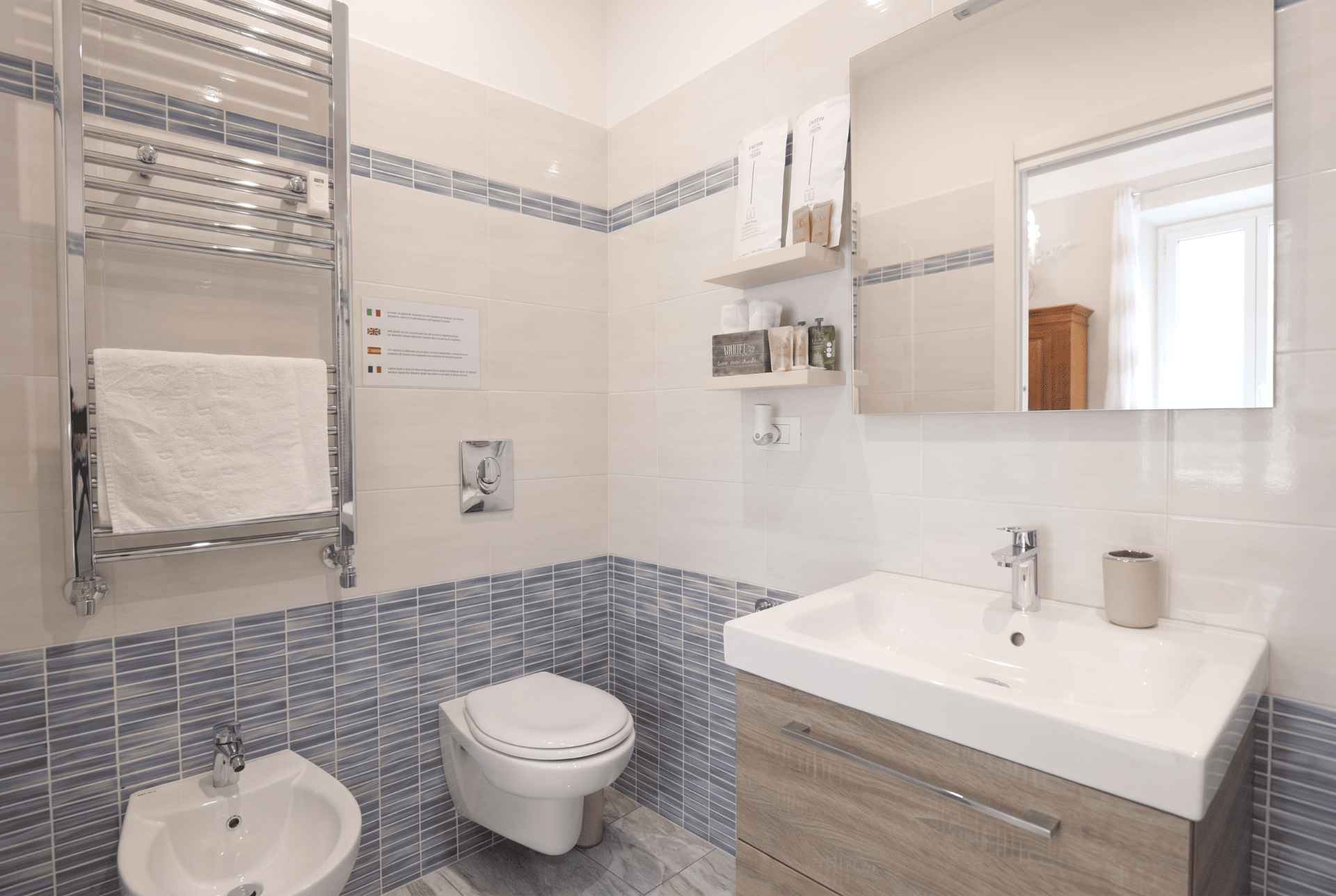 Bagno privato di Cachemire: lavabo su mobile in legno, specchio, WC e bidet, rivestimento chiaro con decoro blu