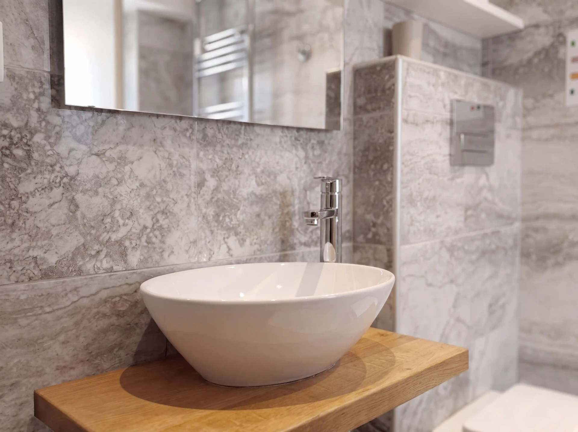Bagno privato di Cannella: lavabo d’appoggio su piano in rovere, specchio e rivestimento in pietra grigia