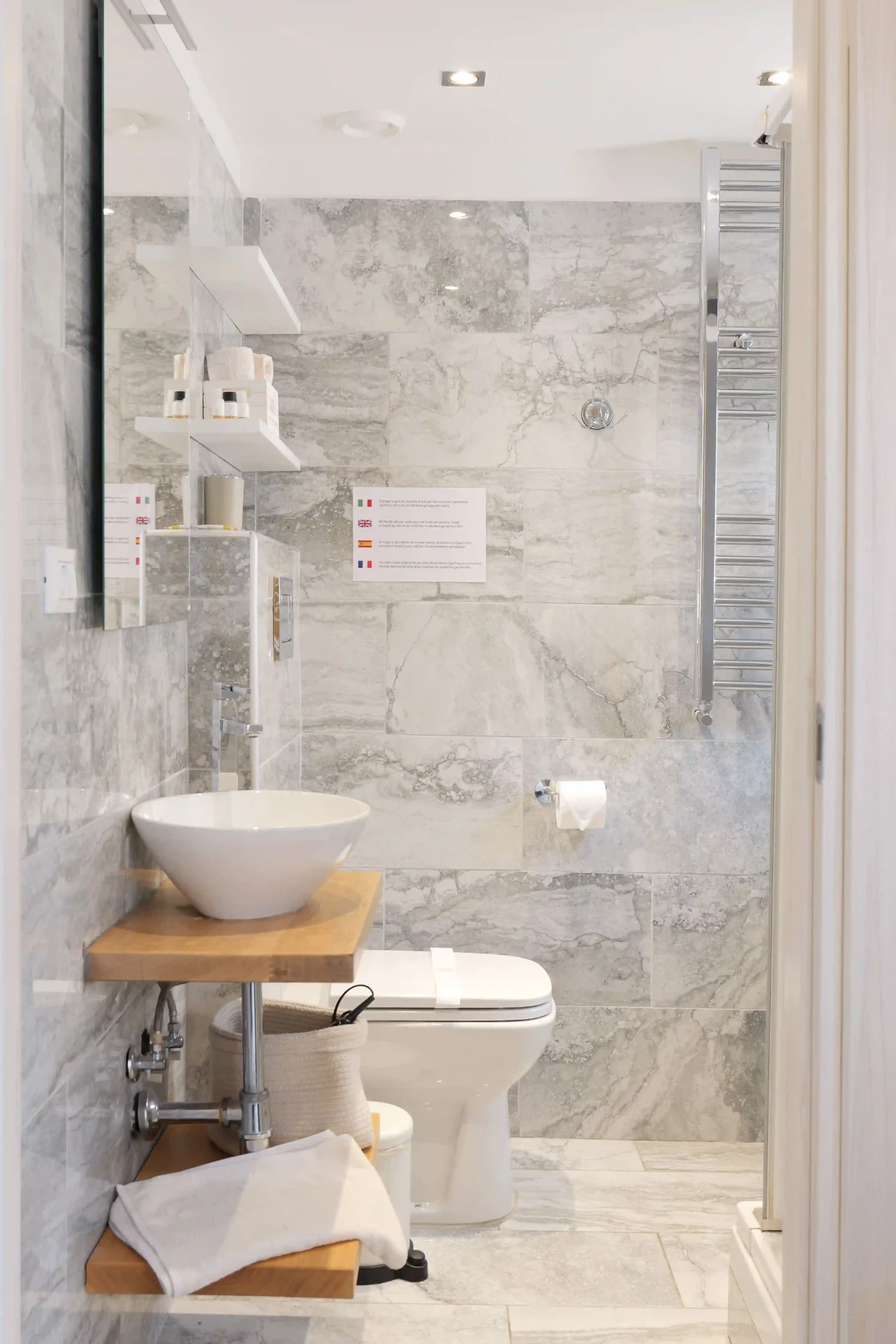 Bagno di Cannella visto dall’ingresso: lavabo su mensola in rovere, WC, scalda-salviette e doccia con rivestimento in pietra