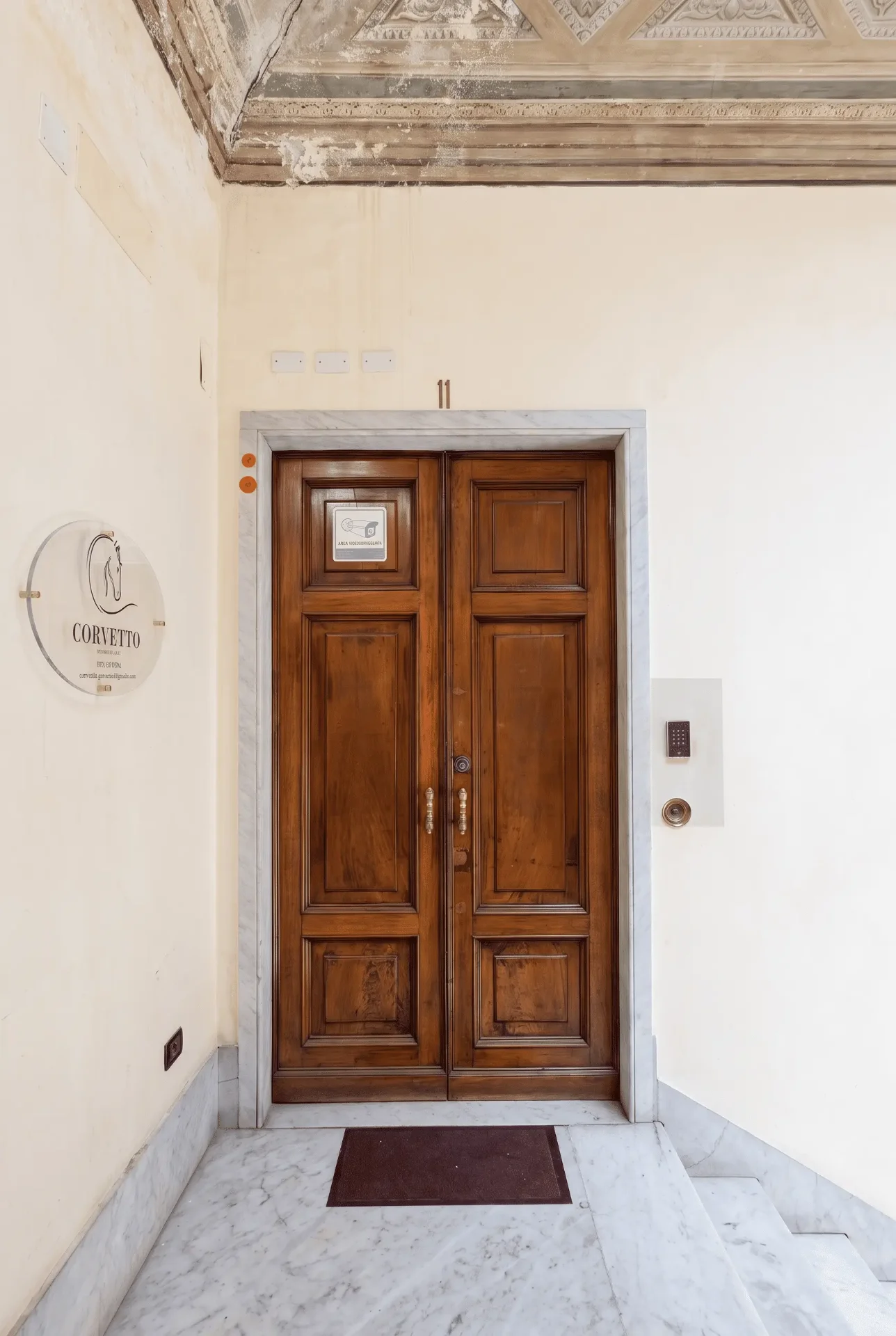 Portone in legno all’ingresso di Corvetto, con pavimento in marmo e soffitto decorato del palazzo