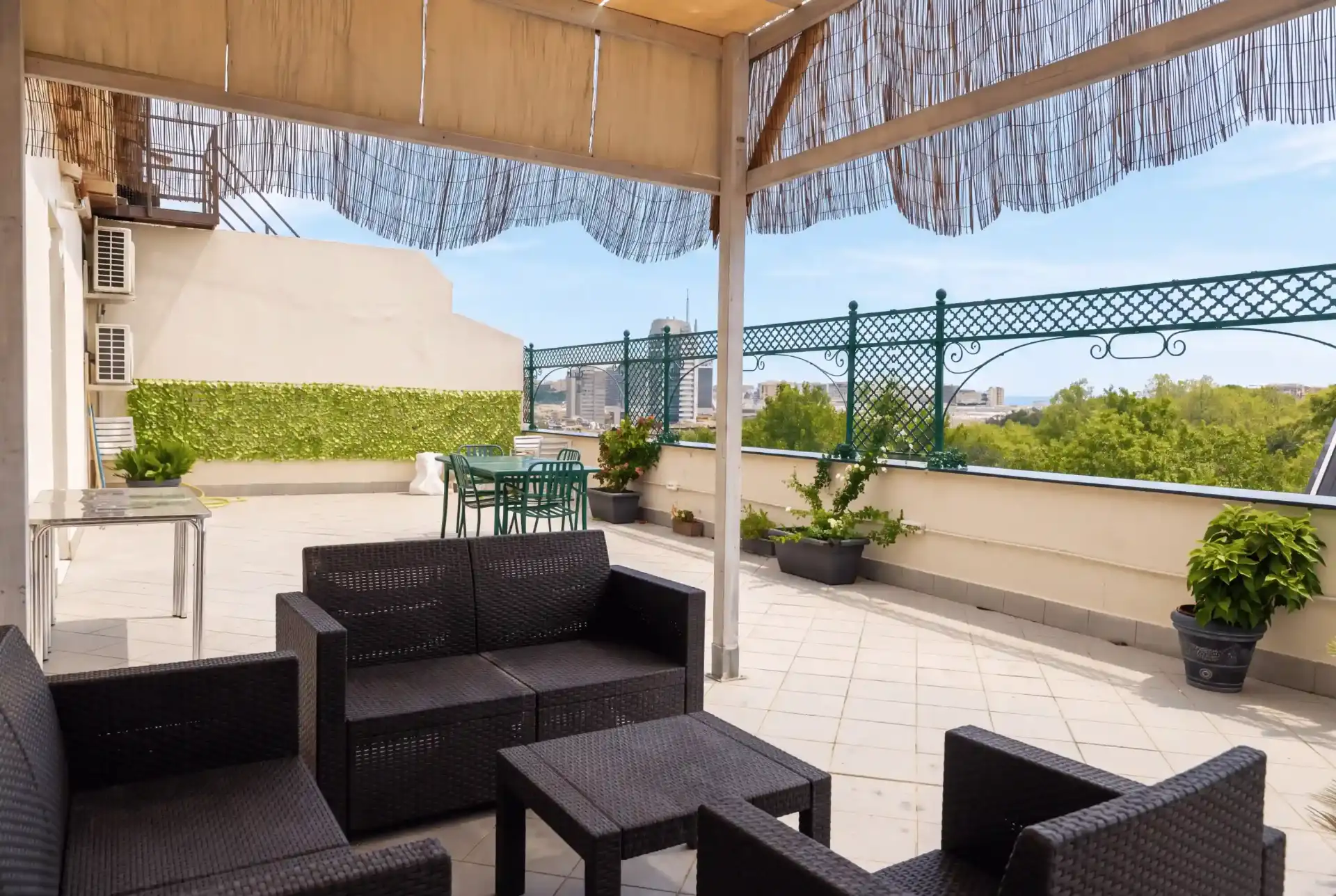 Terrazzino di Corvetto con divani intrecciati, tavolini, piante e ringhiera verde affacciata sulla città