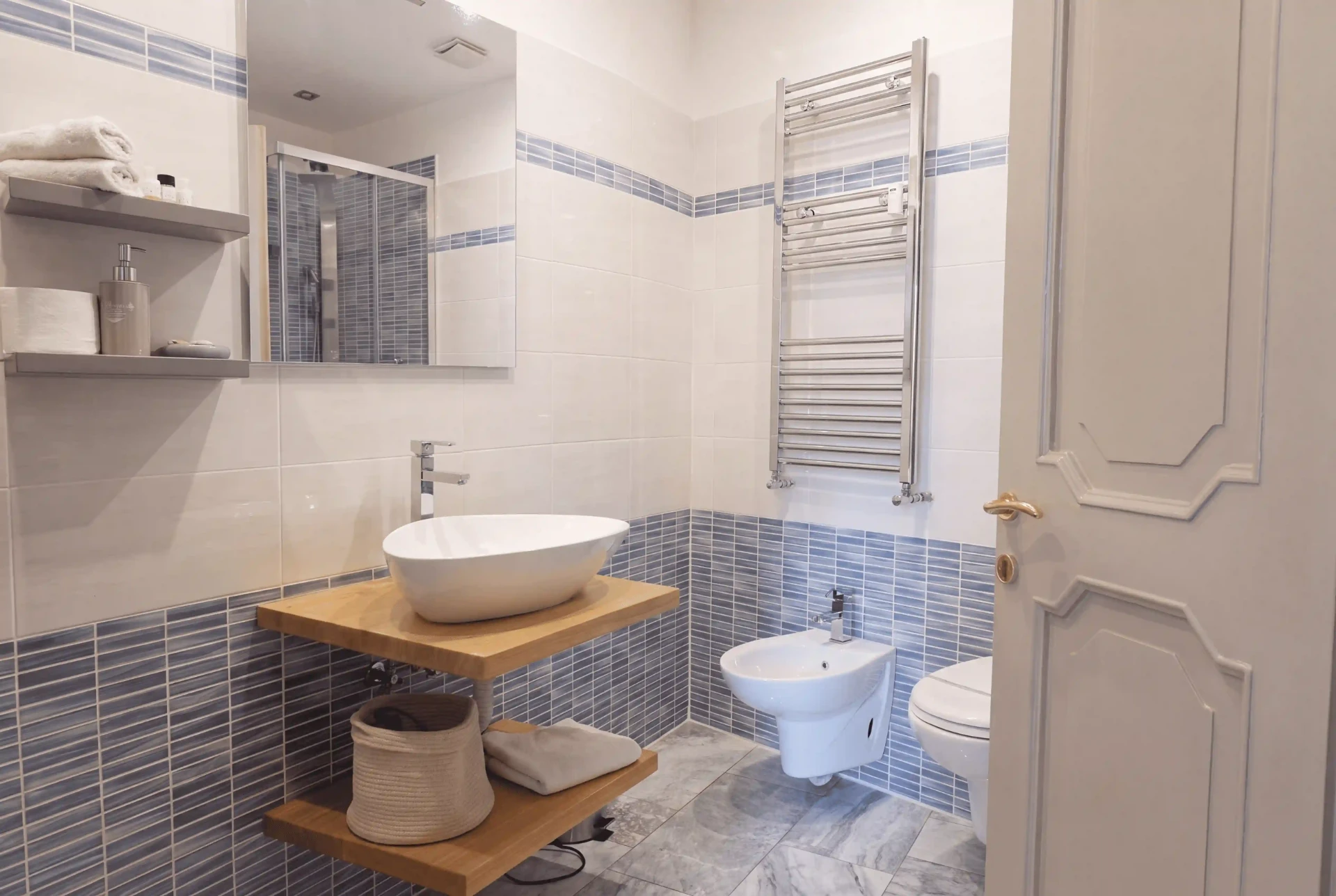 Bagno privato di Cipria: lavabo d’appoggio su mensole in rovere, bidet, scalda-salviette e greca di mosaico blu